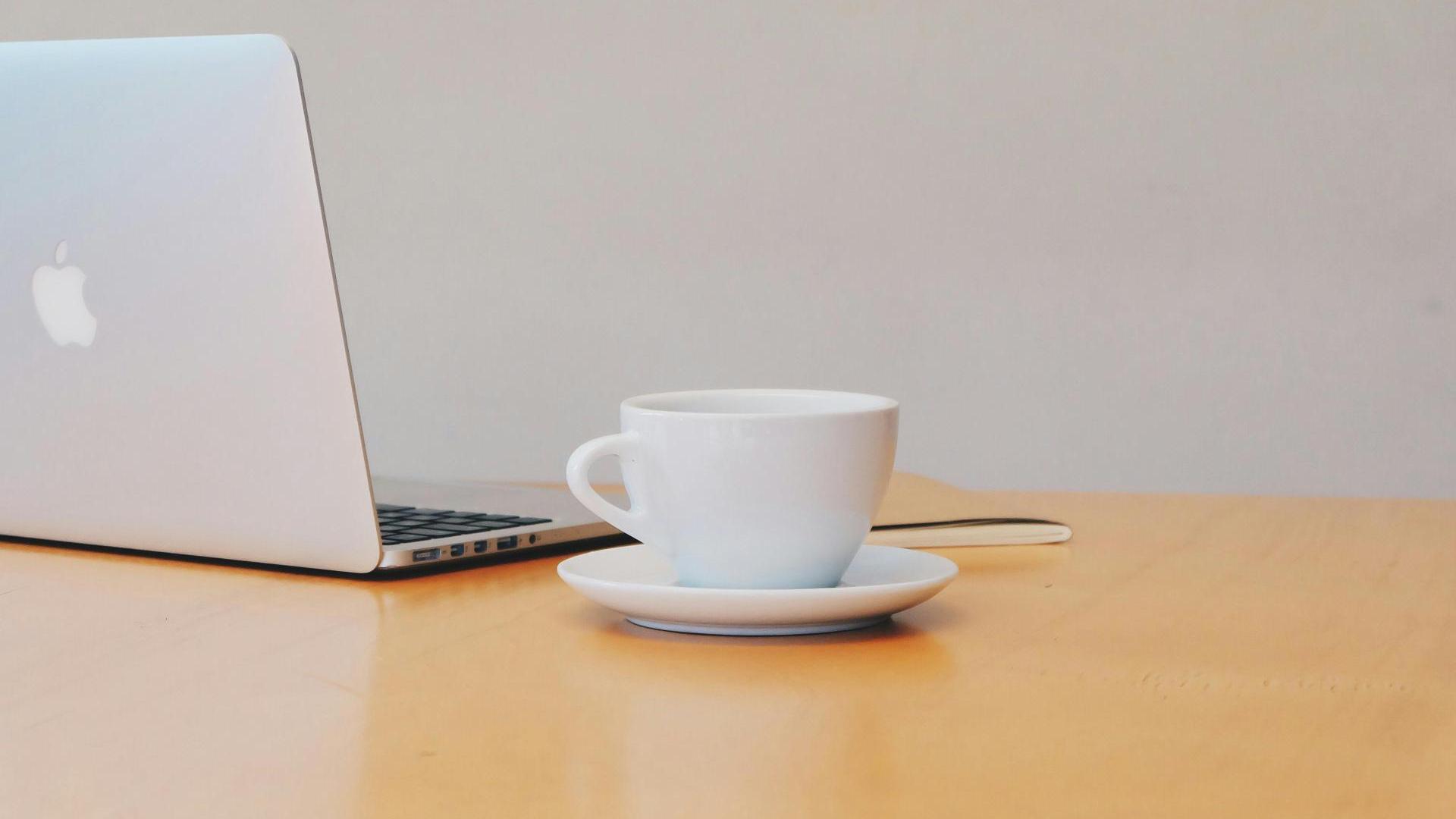 Tietokone ja kahvikuppi pöydällä.